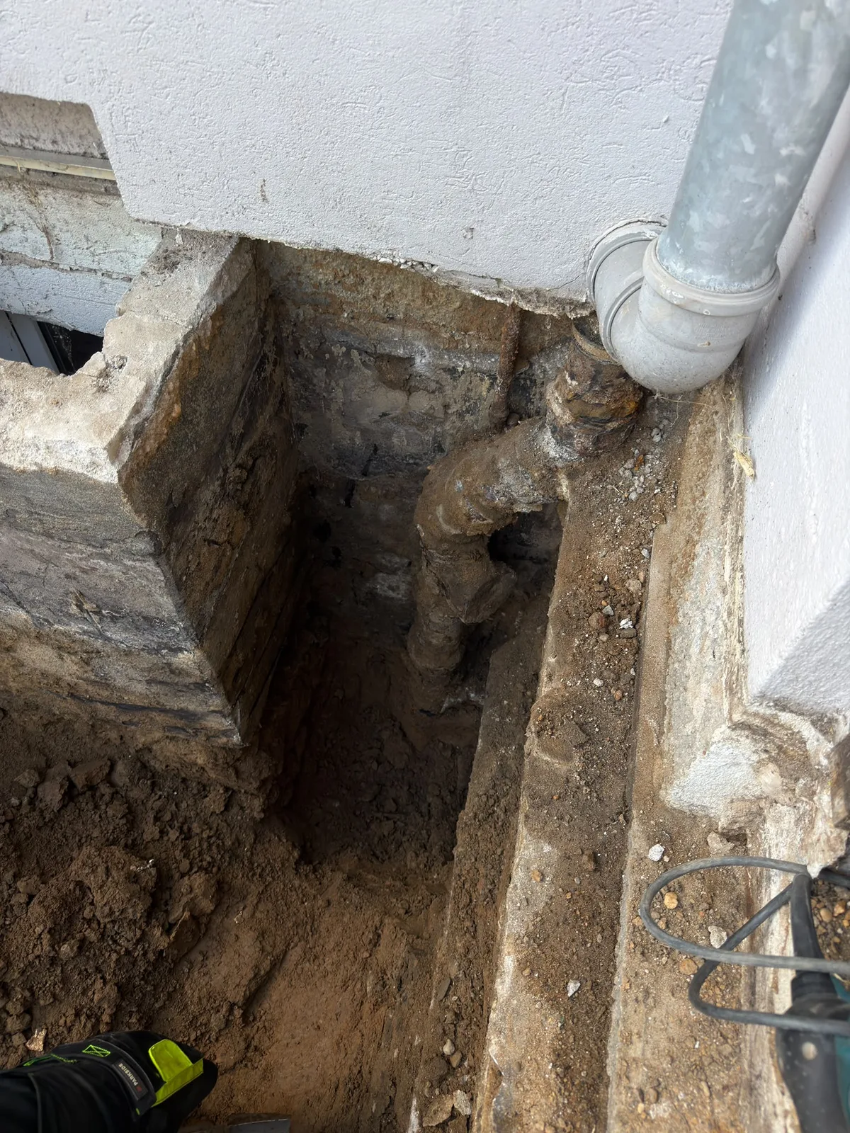 Altes, verrostetes Regenwasserrohr im Graben am Fundament freigelegt